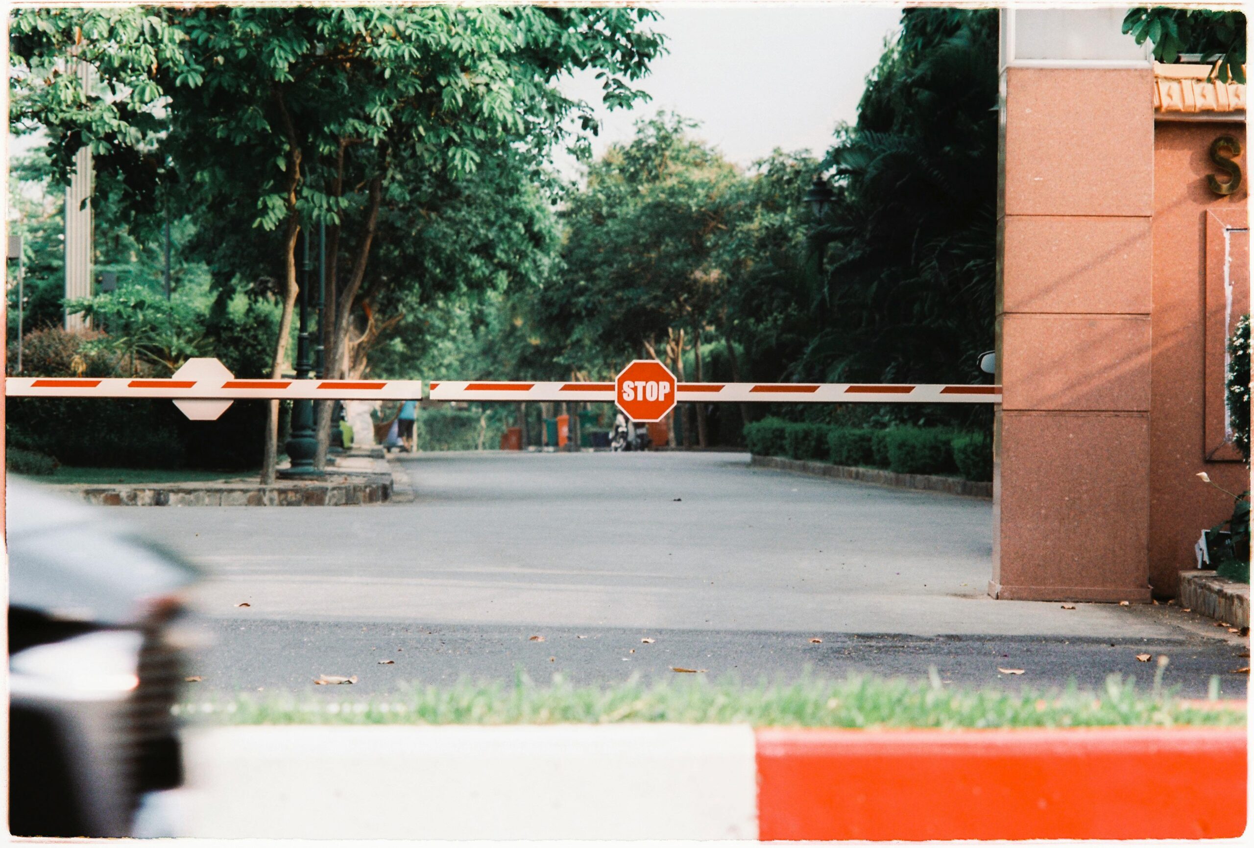 why-choose-us A stop barrier closes off a city street entrance bordered by green trees.